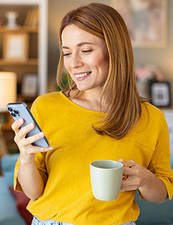 Woman looking at smart phone and drinking a cup of coffee.